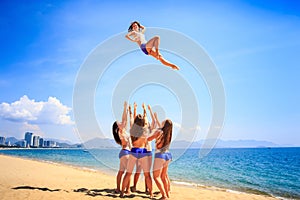 Cheerleaders performs stunt Basket Toss on beach against resort