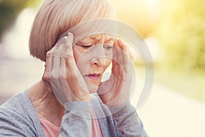 Cheerless elderly woman holding her temples
