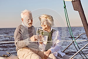 Cheers. Close up of happy senior couple sitting on the side of sail boat or yacht deck floating in sea. Man and woman