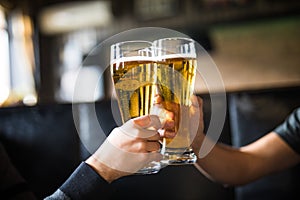 Cheers. Close-up of two men in shirts toasting with beer at the bar counter