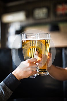 Cheers. Close-up of two men in shirts toasting with beer at the bar counter