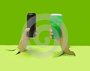 Cheers minimal party concept. Two mans hands holding black can of beer and pint of green alcohol pops out from pastel green floor