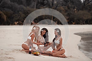 Cheers! Outdoor photo of Appealing Three sexy bikini girls drink wine during a picnic on tropical beach at Maldives island. Slim