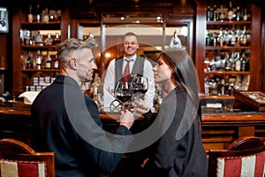 Cheers. Two casual business people in a hotel bar in the evening talking while having two glasses of red wine after