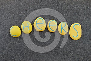Cheers word composed with yellow colored stones over black volcanic sand
