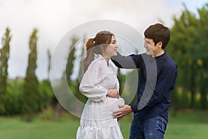 Cheertul married couple is expecting a baby. man embraces his pregnant wife in park