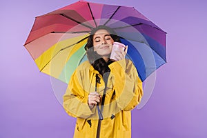 Cheery brunette woman in yellow raincoat holding umbrella