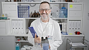 Cheery middle age man with grey hair, confidently working as a scientist at the lab, holding clipboard and smiling with joy inside