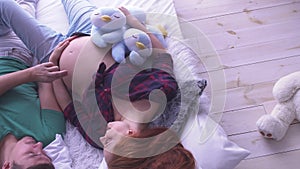 Cheery pregnant woman with long hair and her husband lying in the bed. Man gently touch belly of wife. Maternity concept