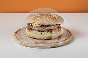 Cheesburgher on wooden plate isolated and centred on white table and orange wall photo