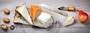Cheese aged in hay, Mimolette cheese, Toma Brusca cheese with pears and walnuts on wood background, top view. photo