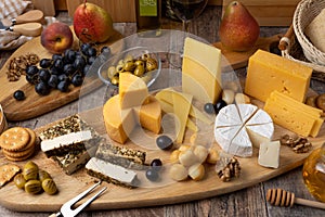 Cheese assorted on a wooden board, rustic style. Several sliced cheeses with pears, peaches, grapes, olives, honey, bread.