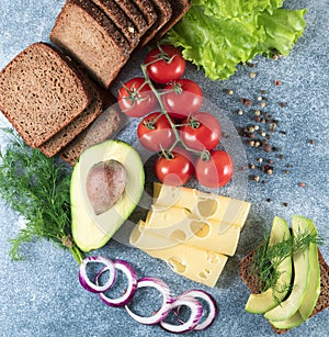 Cheese, avocado, tomato, green sprouts, black bread, salad, onion. Grey background