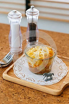 Cheese Baked Penne in glass bowl on wooden plate with salt, pepper, cutlery and miniature horse model