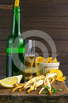 Cheese with beer, lemon and potato chips on dark wooden board. Snack on fish with beer. Front views, close-up