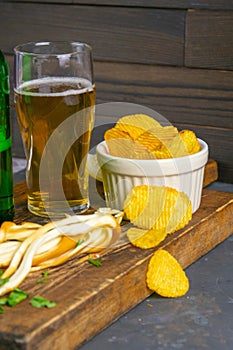 Cheese with beer, lemon and potato chips on dark wooden board. Snack on fish with beer. Front views, close-up