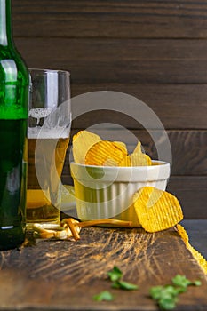 Cheese with beer, lemon and potato chips on dark wooden board. Snack on fish with beer. Front views, close-up