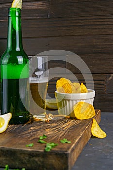 Cheese with beer, lemon and potato chips on dark wooden board. Snack on fish with beer. Front views, close-up