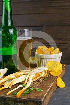 Cheese with beer, lemon and potato chips on dark wooden board. Snack on fish with beer. Front views, close-up