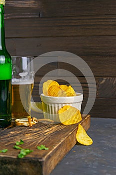 Cheese with beer, lemon and potato chips on dark wooden board. Snack on fish with beer. Front views, close-up