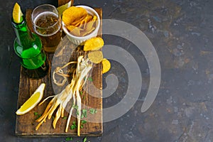 Cheese with beer, lemon and potato chips on dark wooden board. Snack on fish with beer. Top views with clear space