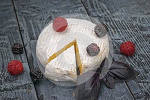 Cheese with berries and blue basil leaves on a wooden trunk