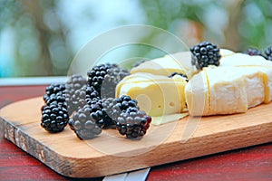 Cheese with blueberries on a wooden board. Sliced cheese with berries