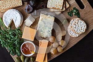 Cheese board serving with figs, caper berries, jam, parsley and pickled onions. Top view photograph with copy space -