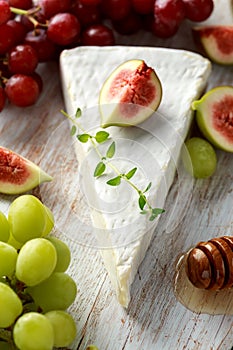 Cheese brie with figs, green and red grape and honey on white wooden board