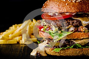 Cheese burger with grilled meat, cheese, tomato and potatoes on dark wooden surface. Ideal for advertisement. Close-up