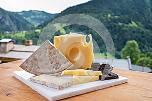 Cheese collection, Swiss cow cheese emmental, tomme and dark chocolate and mountains village in Apls on background