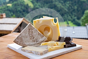 Cheese collection, Swiss cow cheese emmental, tomme and dark chocolate and mountains village in Apls on background