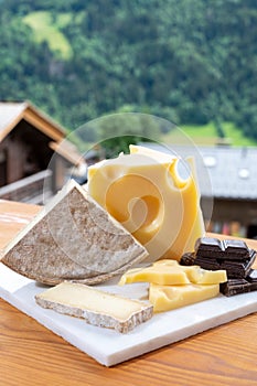 Cheese collection, Swiss cow cheese emmental, tomme and dark chocolate and mountains village in Apls on background