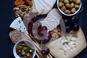 Cheese,cracker,grape,nuts on a black background