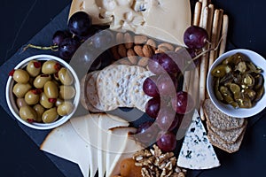 Cheese,cracker,grape,nuts on a black background