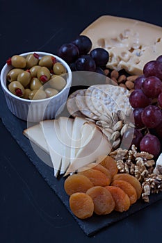 Cheese, crackers, grape, nuts on a black background