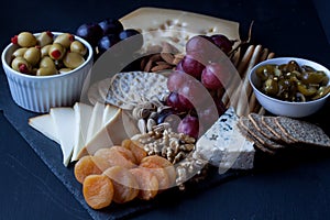 Cheese, crackers, grape, nuts on a black background