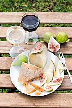 Cheese, figs and glasses of red and white wine on a wooden table.