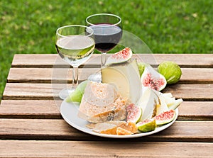 Cheese, figs and glasses of red and white wine on a wooden table.