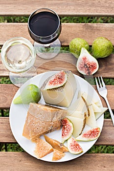 Cheese, figs and glasses of red and white wine on a wooden table.