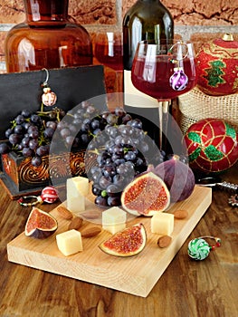 Cheese and figs on a wooden board, red wine in a glass, grape and Christmas attributes around