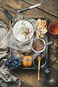 Cheese, fruit, wine set in wooden tray over rustic background