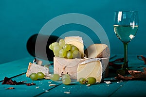 Cheese, grapes and wine on wooden cyan surface.
