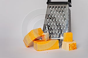 Cheese grater and blocks of cheddar cheese on solid background