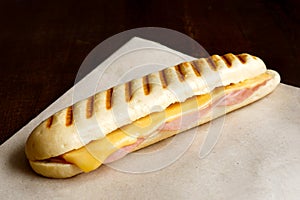 Cheese and ham toasted panini. On brown paper and wood.