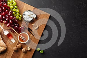 Cheese head, bunch of grapes, honey, nuts and wineglass on wooden board and black background