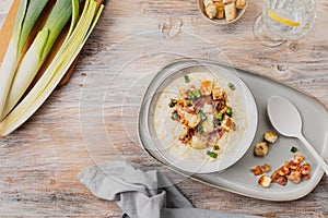 Cheese leek soup with croutons and bacon in a bowl on a wooden table.