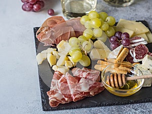 Cheese and meat wine snack set. Variety of cheese, salami, prosciutto, bread sticks, honey, grapes and two glasses with white wine