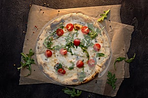 Cheese pizza with paper and tomato on dark wooden background top view