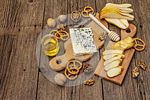 Cheese plate antipasti with smoked and blue cheese, crackers, honey, walnuts and ripe pear. Traditional snack recipe idea. Wooden